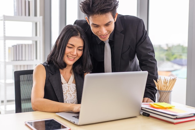 Due uomini d'affari che lavorano insieme con il sorriso sul viso utilizzando il laptop in ufficio