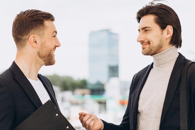 Due uomini d'affari felici moderni che discutono qualcosa sullo sfondo di uffici ed edifici urbani