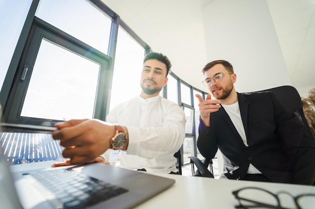 Due uomini d'affari multietnici che lavorano su un computer portatile in ufficio