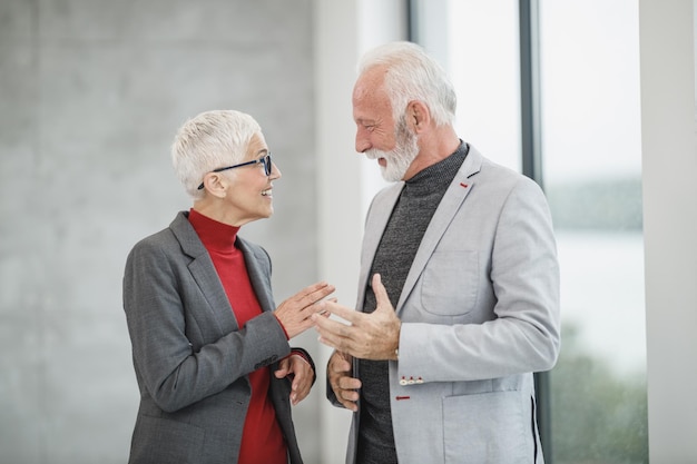 Due uomini d'affari senior sorridenti che camminano e parlano in un ufficio moderno.