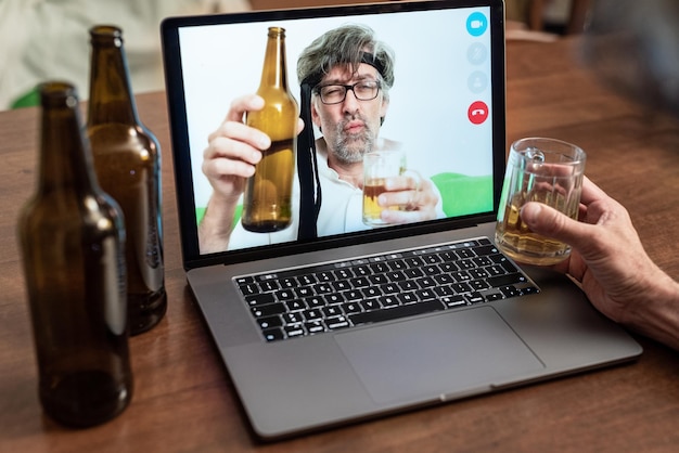 Due uomini esagerano bevendo birra e ubriacandosi durante una videochiamata, vecchi amici che brindano tramite una chiamata al computer