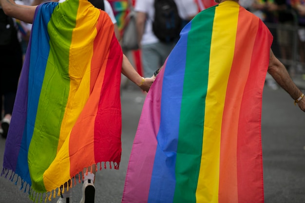 Due uomini gay avvolti in bandiere del gay pride che si tengono per mano l'uno con l'altro