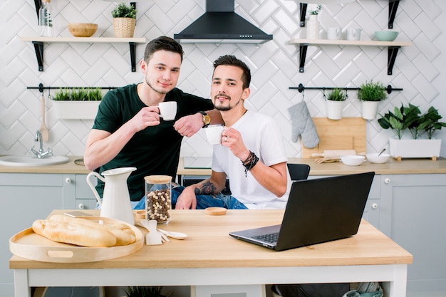 Due uomini gay felici nell'homewear che spendono mattina nella cucina. Uomini gay felici che mangiano prima colazione a casa la mattina