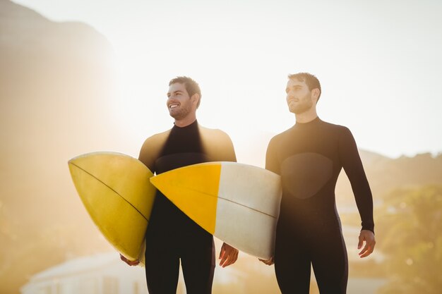 Due uomini in mute umide con una tavola da surf in una giornata di sole