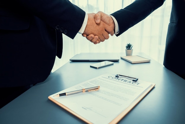 Due uomini si stringono la mano sopra un contratto con una penna su una scrivania.