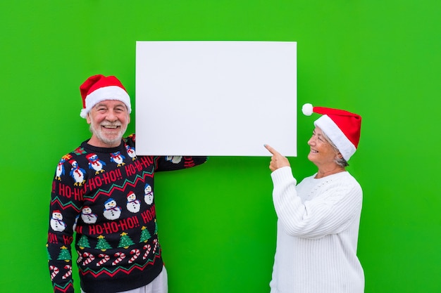 Due uomini vecchi e maturi che tengono uno spazio vuoto o un grande scheet con uno spazio di copia per scrivere il tuo testo - vestiti di natale e sfondo verde