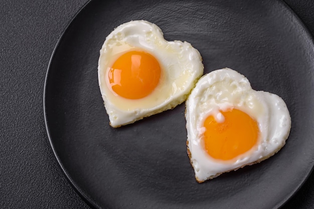 Due uova fritte a forma di cuore su un piatto di ceramica nera su uno sfondo di cemento scuro