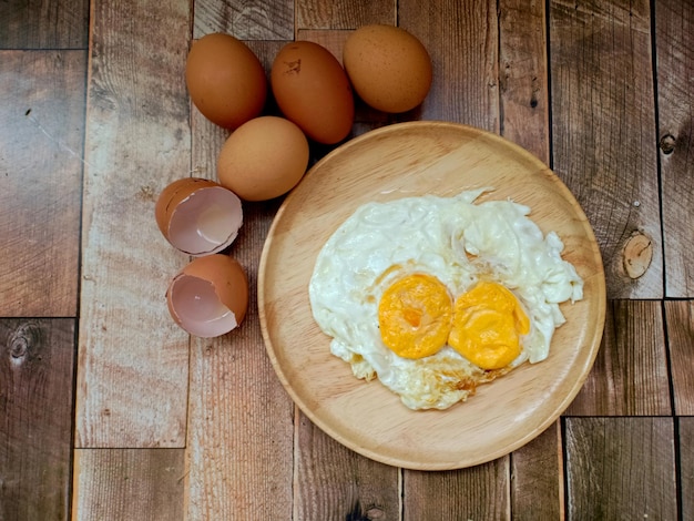 Due uova fritte su un piatto di legno con un gruppo di uova fresche su uno sfondo di legno