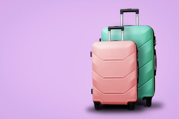 Due valigie su ruote su uno sfondo viola. Concetto di viaggio, un viaggio di vacanza, una visita ai parenti. Colore rosa e verde