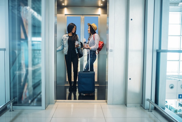 Due viaggiatori femminili con bagagli in ascensore dell'aeroporto. Passeggeri con bagaglio in aerostazione