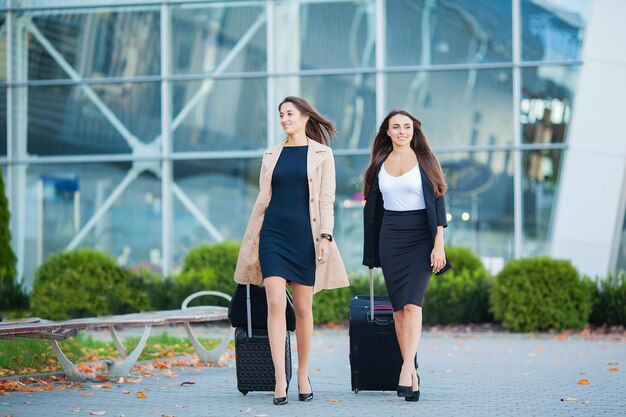 Due viaggiatrici che camminano con i bagagli vicino all'aeroporto.