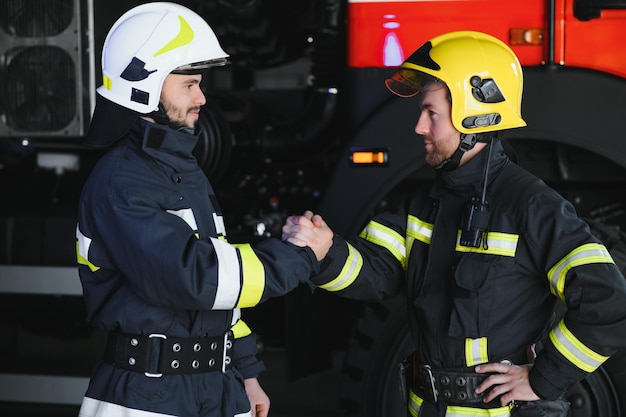 Due vigili del fuoco in indumenti protettivi in caschi con stretta di mano amichevole per i vigili del fuoco