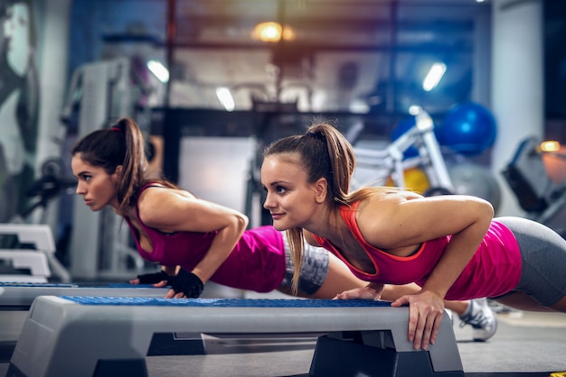 Due womans in una palestra facendo flessioni su uno stepper. Forte e dedicato.