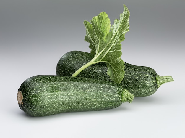 Due zucchine verdi fresche e foglie su uno sfondo bianco. isolato