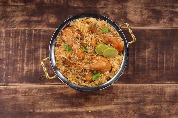 Dum pollo biriyani, immagine ravvicinata del Kerala-Thalassery biriyani che è mescolato con masala e di colore giallo disposto in una ciotola di rame e guarnito con fette di limone poste su legno