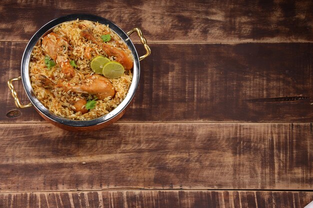 Dum pollo biriyani, immagine ravvicinata del Kerala-Thalassery biriyani che è mescolato con masala e di colore giallo disposto in una ciotola di rame e guarnito con fette di limone poste su legno