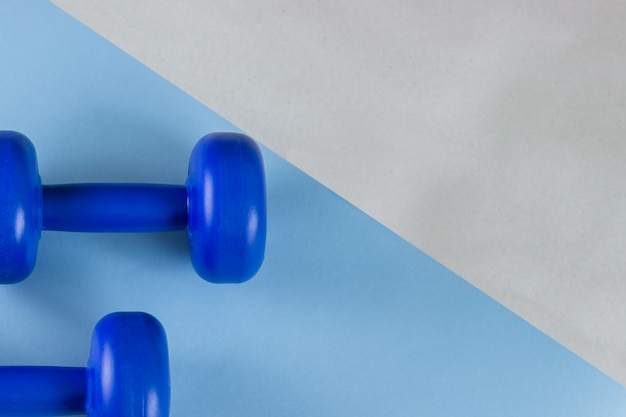 Dumbbells blu luminosi su una priorità bassa blu. Si preoccupa per il corpo. Posto vuoto per il testo