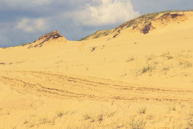 Dune di sabbia tra le nuvole del cielo azzurro, la pista di un'auto sulla sabbia