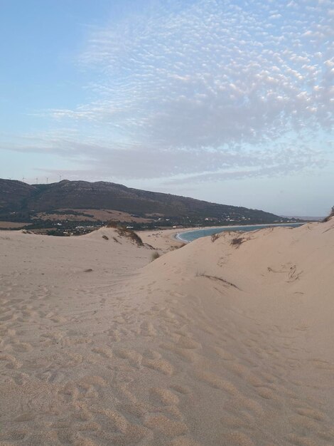 Dune vicino all'oceano con montagne e nuvole