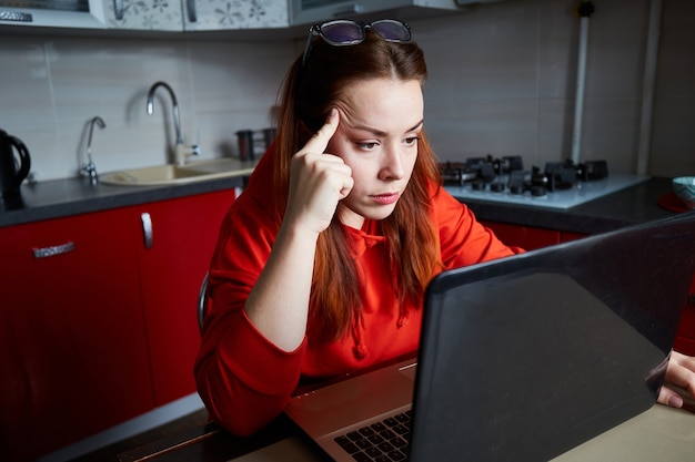 Duro lavoro a distanza Studente stanco con una giacca rossa che lavora e cerca informazioni su un laptop a casa