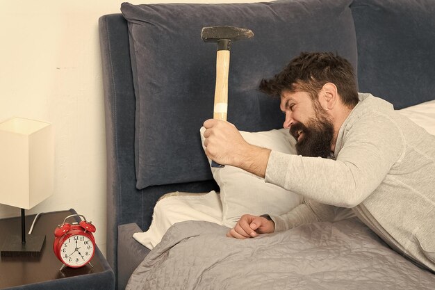 Duro weekend Uomo sveglio insoddisfatto della sveglia che suona Dormire più a lungo Concetto di sonno sano uomo barbuto hipster vuole dormire odio il rumore della sveglia Il ragazzo irritato distrugge l'orologio fastidioso