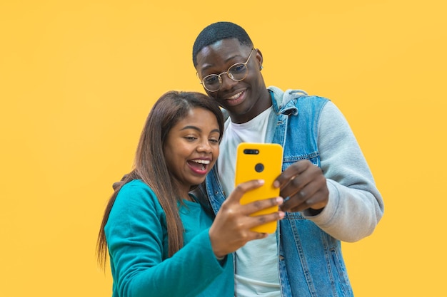 Eccitata coppia afroamericana guardando lo schermo dello smartphone insieme isolato su sfondo giallo