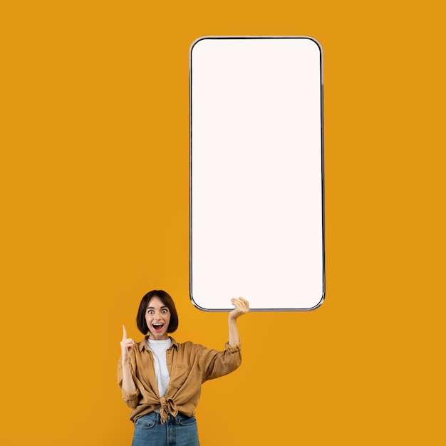 Eccitata giovane donna caucasica che punta allo smartphone con schermo bianco vuoto che consiglia l'app mobile