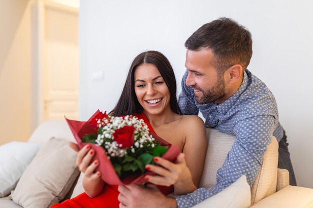 Eccitata giovane donna che riceve un bouquet inaspettato di rose rosse dal marito a casa amorevole fidanzato generoso che fa una sorpresa romantica alla fidanzata attraente in occasione di San Valentino