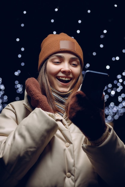 Eccitata giovane donna in capispalla che celebra il successo e legge buone notizie sul cellulare in inverno