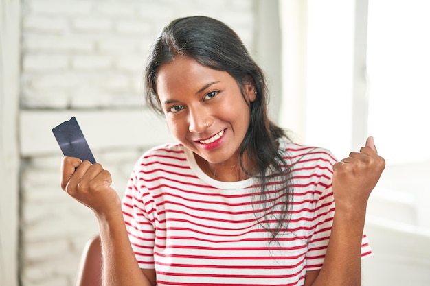 Eccitata giovane donna indiana che festeggia con la carta di credito in mano