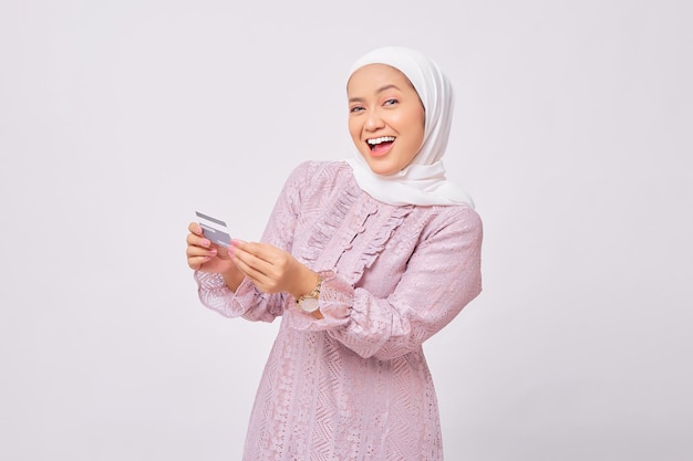 Eccitata giovane donna musulmana asiatica che indossa hijab e abito viola ha ricevuto l'approvazione per accettare carte di credito isolate su sfondo bianco studio