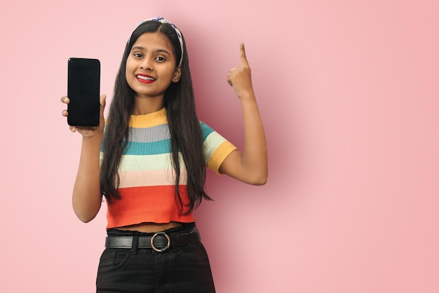 Eccitata giovane ragazza asiatica indiana che tiene il telefono cellulare e punta il dito verso l'alto creando soluzioni geniali isolate con spazio di copia mockup