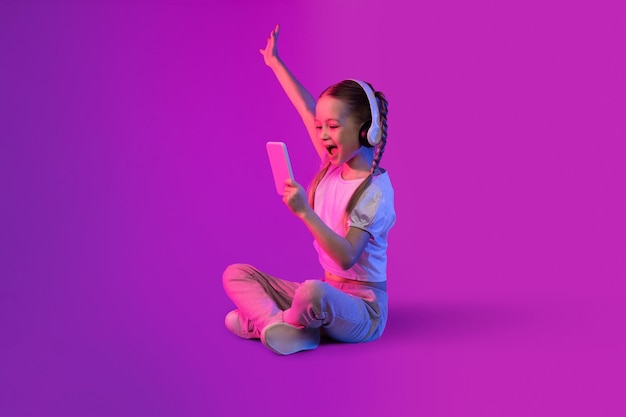 Eccitata ragazza preteen utilizzando cuffie e smartphone su sfondo colorato