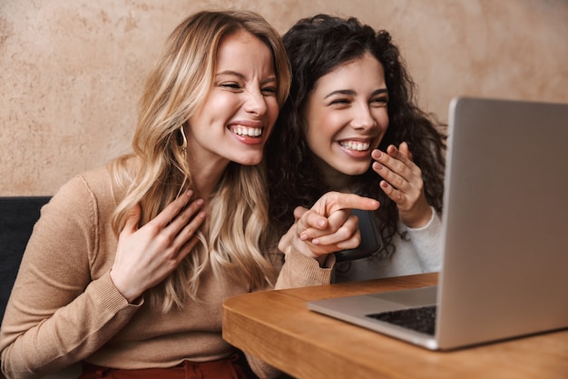 eccitati felici ragazze graziose amiche sedute al bar utilizzando il computer portatile puntato