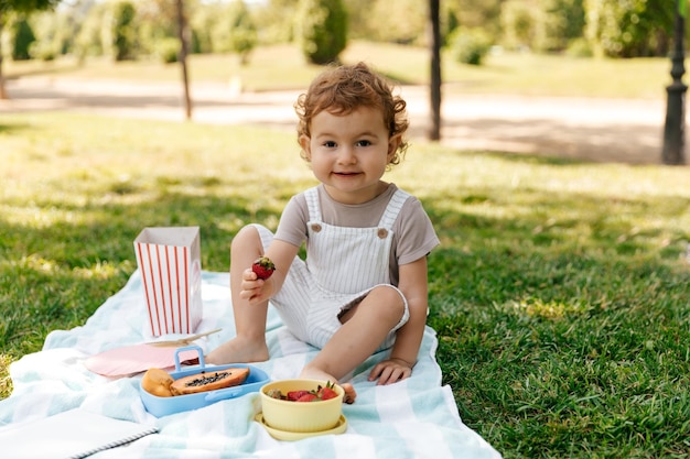 Eccitato adorabile bambino sorridente che si trova sul prato nel parco e si gode la giornata estiva alla luce del sole