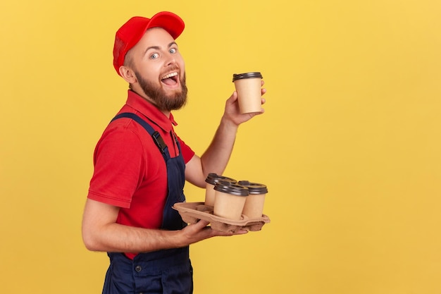 Eccitato fattorino stupito in piedi con caffè da asporto e bere bevande calde