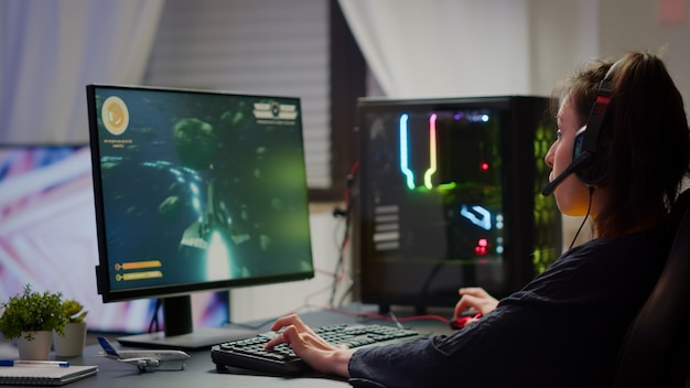 Eccitato giocatore professionista di esport che celebra la vittoria del campionato, donna che vince il videogioco sparatutto spaziale. Campionato di streaming live di tornei online di cyber gaming pro utilizzando un potente computer RGB