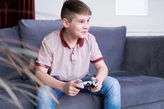 Eccitato giovane adolescente ragazzo giocatore di giocare ai videogiochi con il joystick, seduto sul divano a casa.