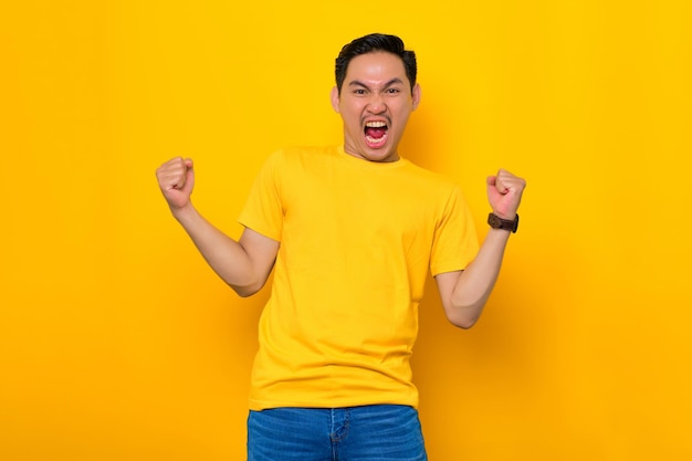 Eccitato giovane asiatico in maglietta casual che celebra il successo con il pugno alzato isolato su sfondo giallo Concetto di stile di vita delle persone