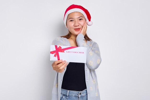 Eccitato giovane donna asiatica 20s in cappello Natale che mostra un buono regalo buono buono carta a disposizione isolato su sfondo bianco per studio Buon Natale Concept