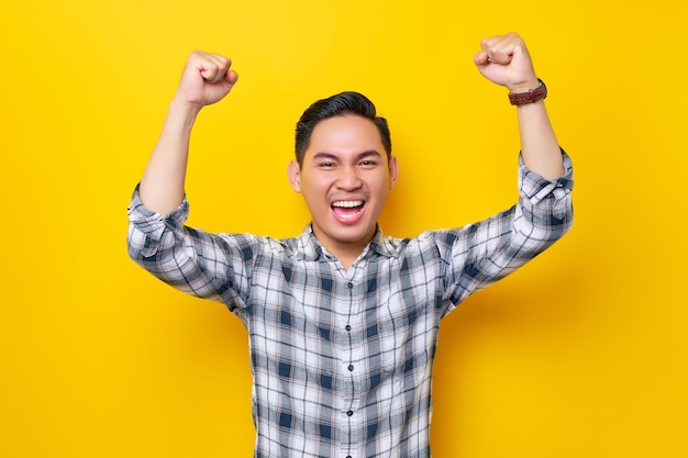 Eccitato giovane uomo asiatico bello che celebra la vittoria o il successo con i pugni sollevati isolati su sfondo giallo Concetto di stile di vita delle persone