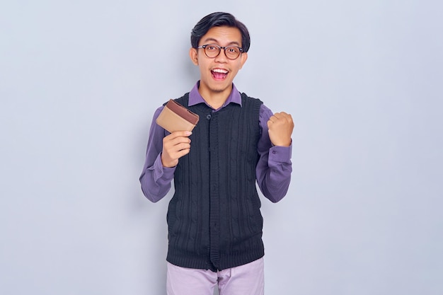 Eccitato giovane uomo asiatico che indossa una camicia con portafoglio marrone e celebra la grande fortuna isolato su sfondo bianco