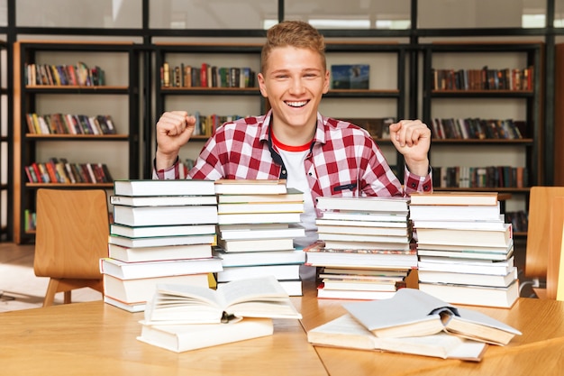 Eccitato ragazzo adolescente seduto in biblioteca