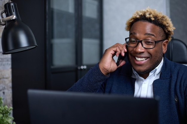 Eccitato uomo d'affari afroamericano sta parlando al telefono sul posto di lavoro