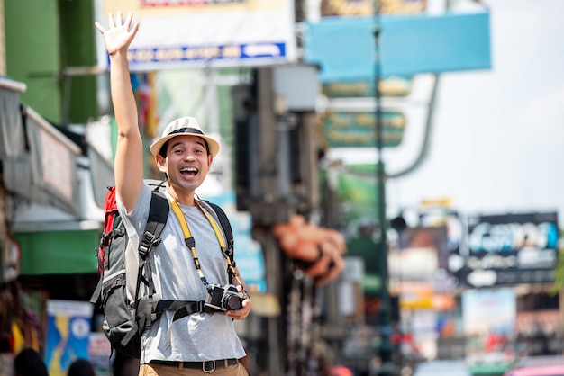 Eccitato uomo turistico asiatico alzando la mano per salutare qualcuno