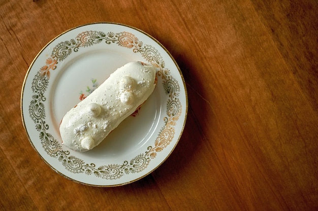 Eclair al cocco con glassa bianca in un piatto bianco su fondo di legno