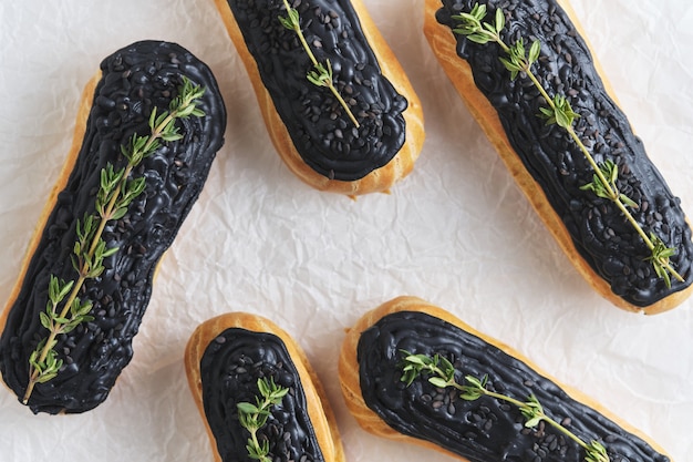 Eclair con crema al pistacchio e glassa nera. Torte decorate con rametti di timo. Dessert sul tavolo da cucina bianco.