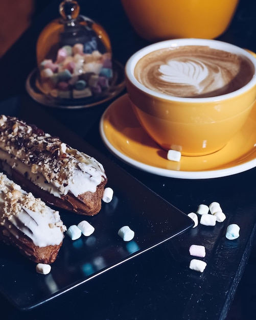 Eclair da dessert tradizionale francese con tazza di caffè al cioccolato bianco e mini marshmallow in un bar o ristorante