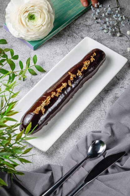 Eclair lunghi fatti in casa con glassa di cioccolato e caffè, decorati con un letto culinario d'oro su un tavolo di pietra grigia. Menù Ristorante