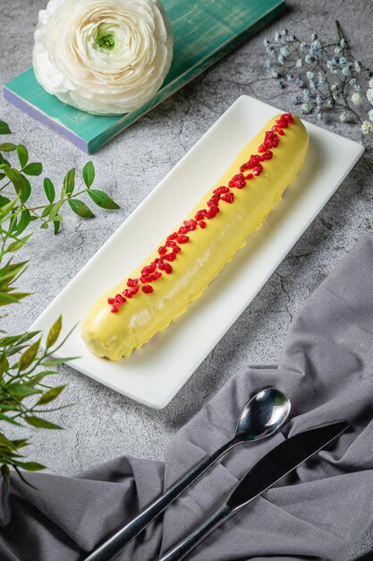 Eclair lunghi fatti in casa in glassa di banana decorati con lamponi su un tavolo di pietra grigia. Menù Ristorante